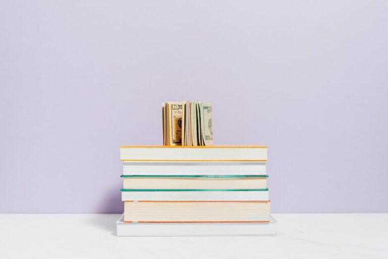 Stack of books with a stack of US dollar bills on top against a pastel background.